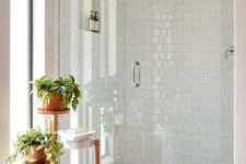a serene white bathroom clad with hexagon and subway tiles, with a niche for storage, a plant stand with potted greenery