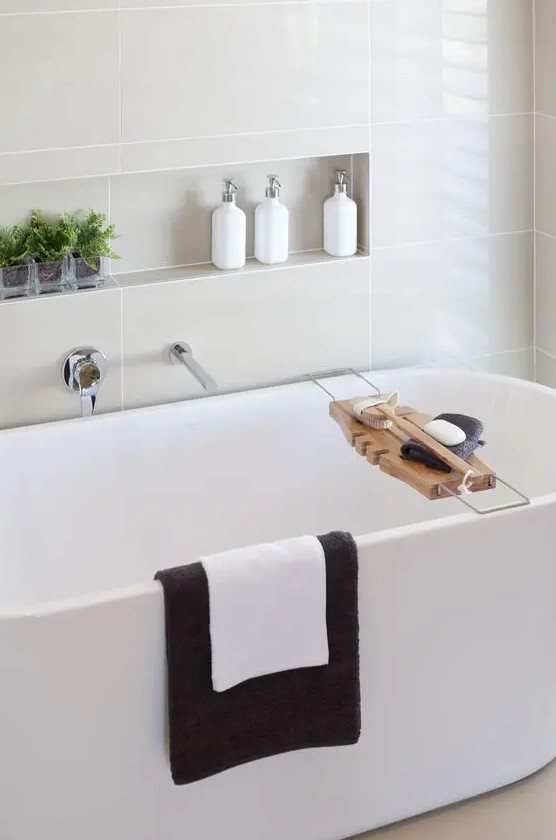 a stylish modern bathroom with an oval tub and a niche shelf over it, with decor and some bathroom stuff