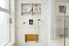 a white marble bathroom with niche shelves used for storage, a folding seat and elegant vintage fixtures