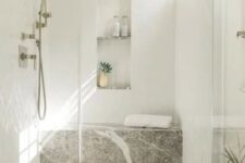 an airy and serene shower space done with herringbone tiles and a stone slab, with an arched niche for storage and decor