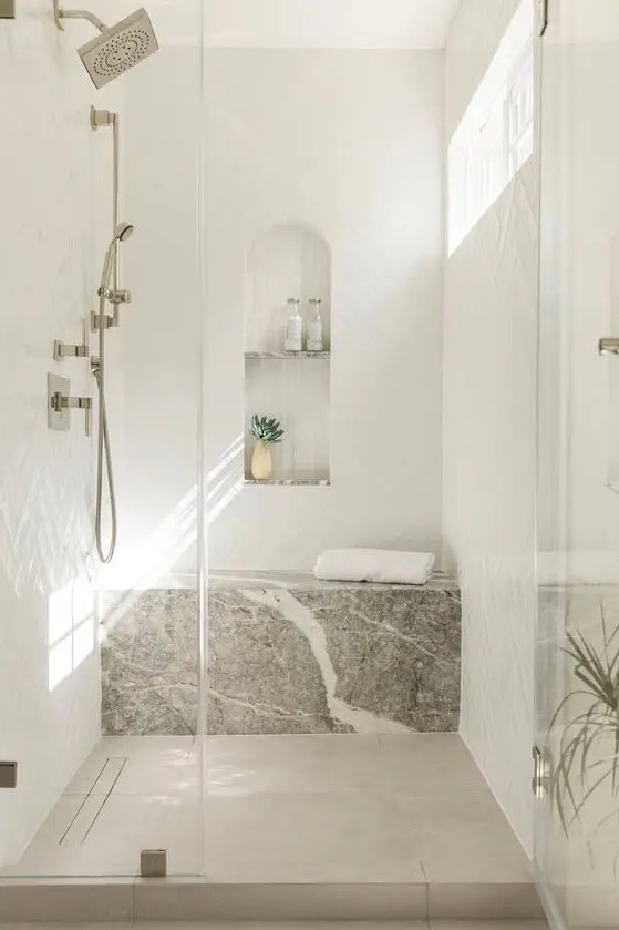 an airy and serene shower space done with herringbone tiles and a stone slab, with an arched niche for storage and decor