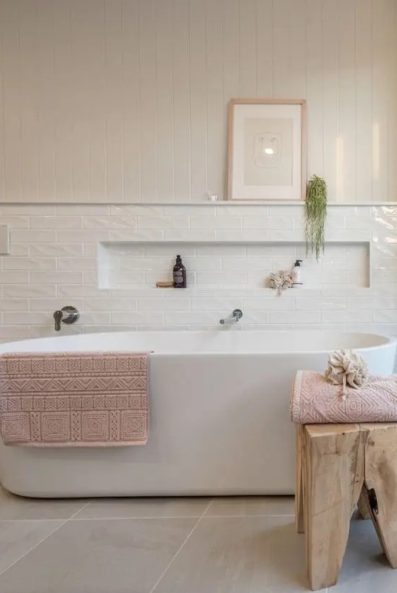 an airy modern bathroom with shiplap and skinny white tiles, an oval tub, a wooden stool and a niche in the tiles for some bathroom stuff