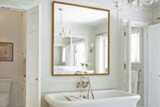 a contemporary bathroom in neutrals, with a large tub, vintage brass fixtures, a large mirror over the tub and a crystal chandelier
