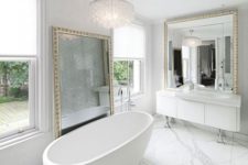 a contemporary luxurious space done in white marble, with two large mirrors in gorgeous frames and a crystal chandelier