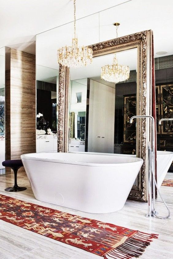 a gorgeous bathroom with a glam chandelier, a mirror wall plus an additional mirror, a free-standing tub and a boho rug