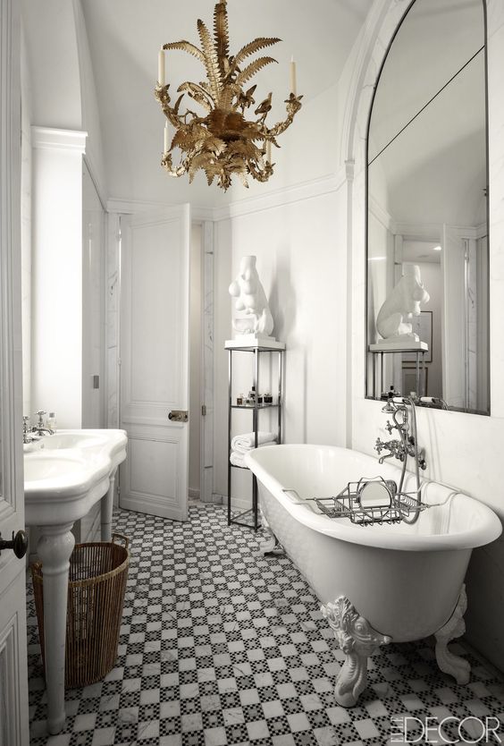 a quirky vintage bathroom with a gorgeous tub, black and white tiles, a gold chandelier and a large mirror over the tub