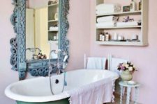 a shabby chic bathroom with pink walls, a green clawfoot tub, a patina ornate frame mirror and a shelf