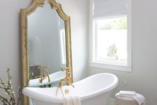 a vintage bathroom in neutrals, with a statement mirror, a vintage chandelier, a retro tub and gold fixtures
