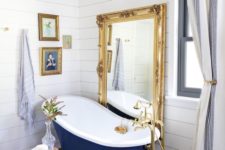 a vintage bathroom of white wood, with a navy clawfoot tub, a crystal chandelier, a mirror in an ornate gold frame