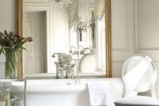 a vintage bathroom with a large tub, an ornate vintage mirror, a crystal chandelier and some refined furniture