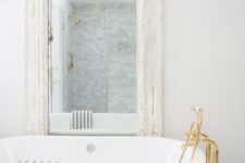 an eclectic bathing space with a white tub, gold fixtures, a vintage mirror in an ornate whitewashed frame