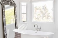an eclectic bathroom in neutrals, an oval tub, a wooden stool, a 3D chandelier and an ornate frame mirror