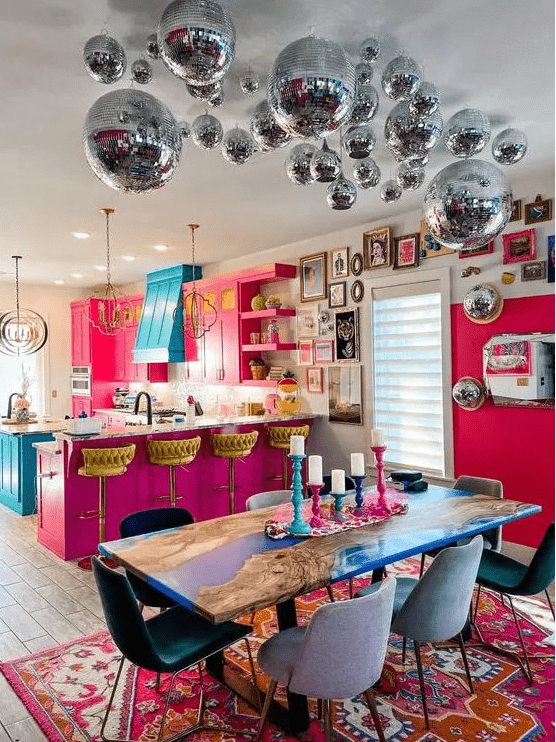 a dopamine decor space with a hot pink kitchen, a turquoise hood and kitchen island, an electric blue table and disco balls over it