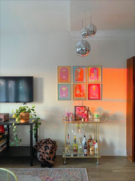 a home bar with a bar cart, a bright gallery wall and disco balls over it is a super cool and dopamine-infusing idea