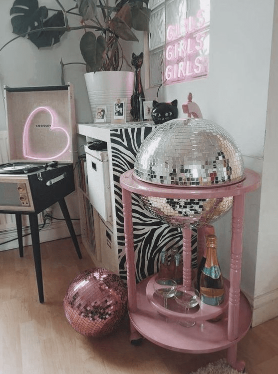 a little home bar styled as a disco ball in a pink stand, with glasses and a bottles and everything else hidden inside