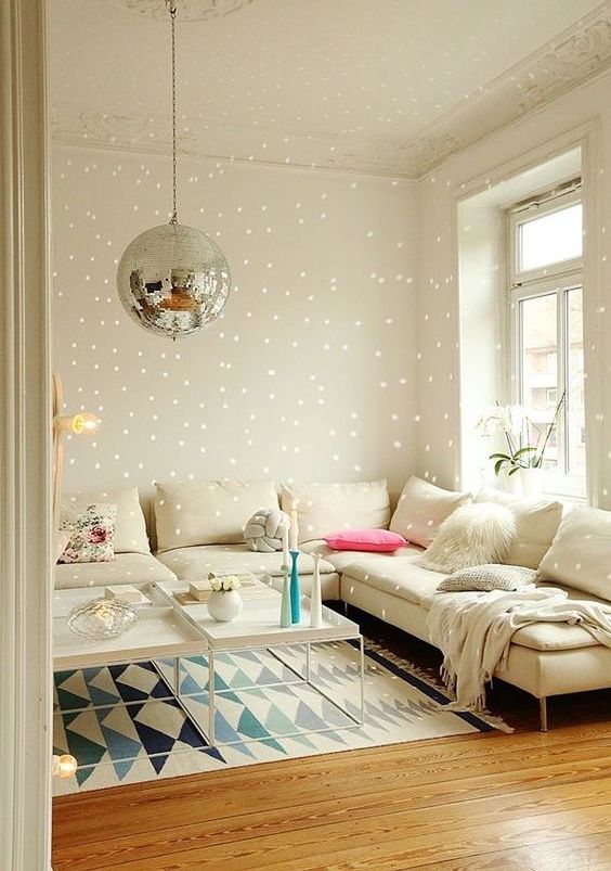 a neutral living room with a creamy corner sofa, coffee tables, printed rugs and a disco ball hanging over the space