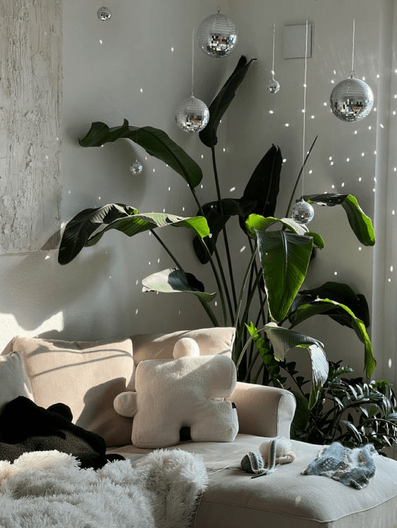 a neutral sofa with neutral pillows, potted plants and an arrangement of disco balls to fill the space with light