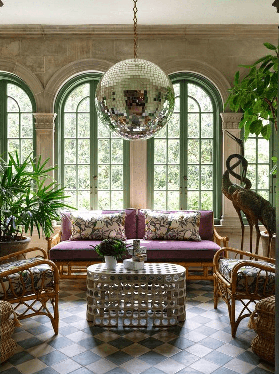 a whimsical living room with arched window, potted plants, rattan furniture, a quirky table and a large disco balls