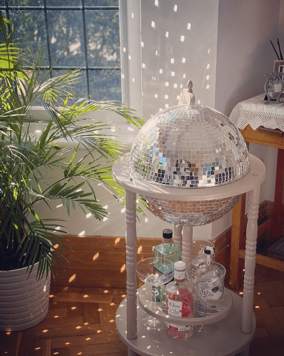 a white bar cart with a disco ball and drinks and bottles is a fun and cool idea to add a party feel to the space