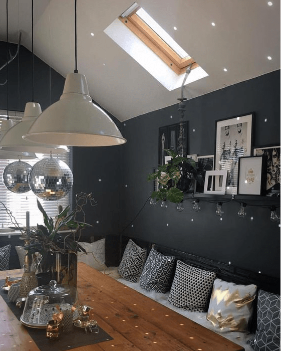 an attic Scandinavian dining room with black walls, a corner sofa with pillows, a table with lamps and disco balls over it