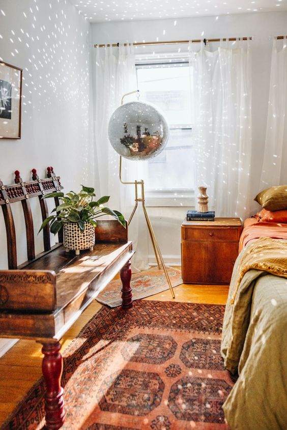 an eclectic boho bedroom with a discao ball, a stained bench, a bed with bold bedding and a bright boho rug