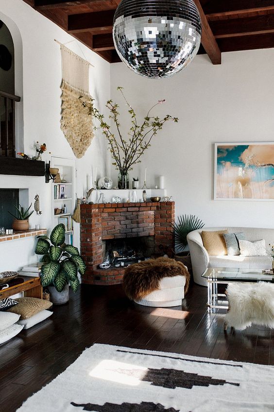 an eclectic living room with a brick fireplace, a creamy sofa, a glass coffee table, a console, some rugs and pillows and a disco ball