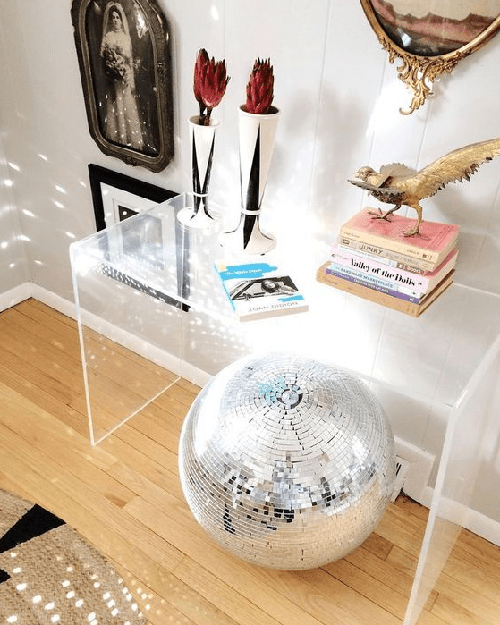 bold home decor with an acrylic console table, a disco ball, some books, a bird figurine, dried flowers in vases