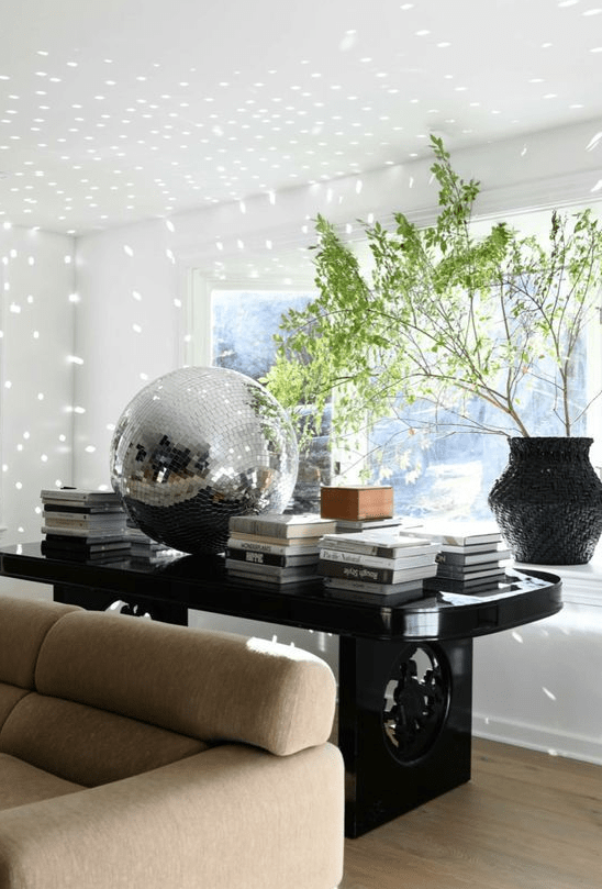 refined decor with a large black table, a lot of coffee tables, greenery in a vase and a large disco ball is amazing