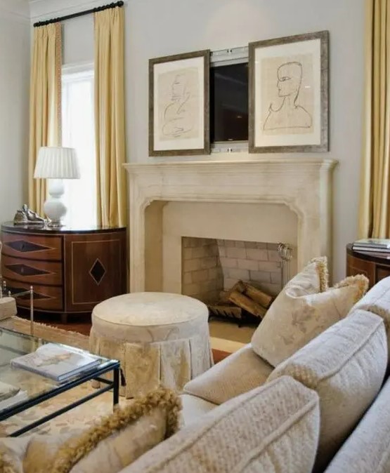a refined modern living room done in neutrals, with a fireplace and an antique mantel, neutral sitting furniture, a TV hidden with two artworks