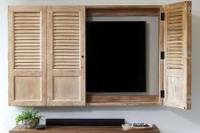 hand crafted shutter doors create the feeling of a window open and hide a wall-mounted TV at the same time adding a rustic feel to the interior