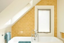 a bright attic bathroom with a yellow tile wall, a free-standing tub, a white hex tile floor and two windows