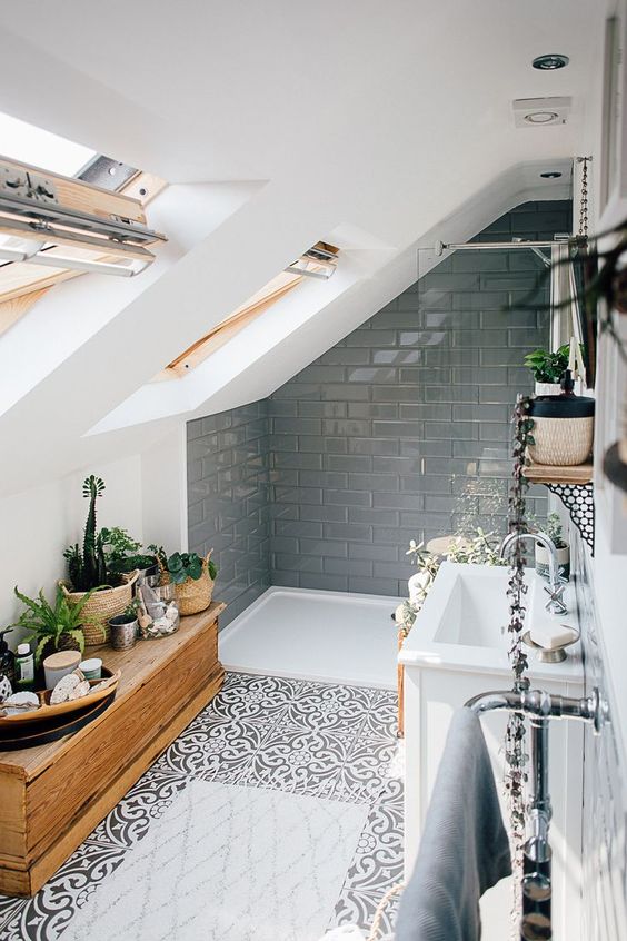 a chic modern bathroom with grey tiles in the shower space, printed tiles on the floor, a wooden chest and skylights