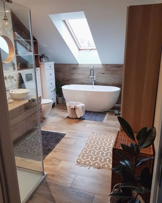 a contemporary attic bathroom clad with wooden panels and tiles, with an oval tub, white and wood furniture and a skylight