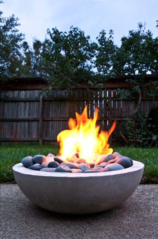 a large modern round fire bowl with oversized pebbles is a chic way to warm up the space