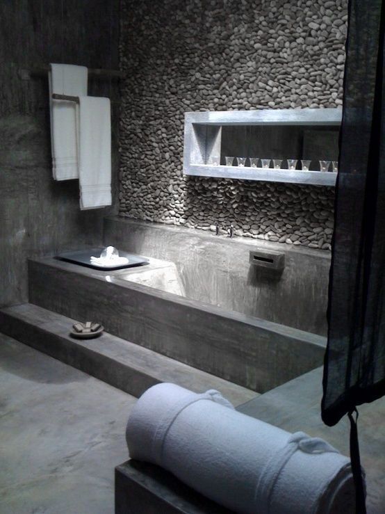 a minimalist concrete bathroom done with a single pebble covered wall for a natural feel