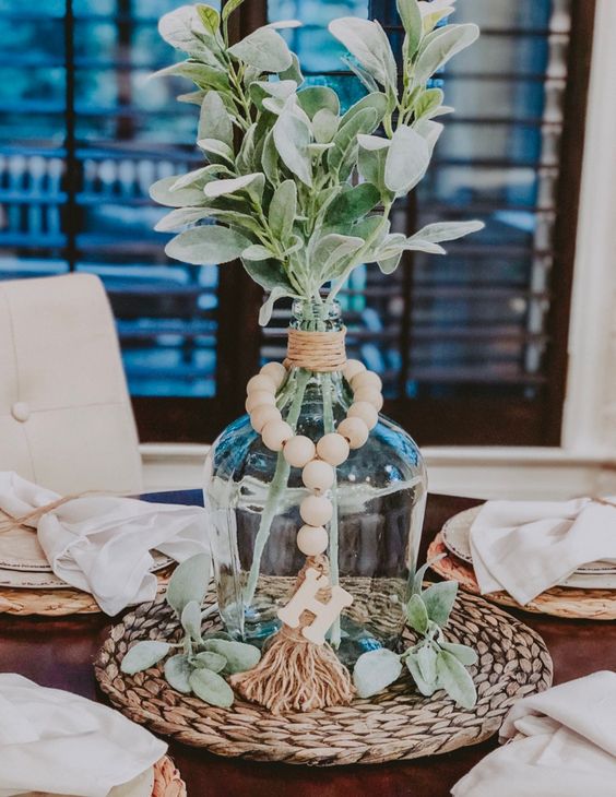 a pretty centerpiece with twine, wooden beads, greenery on a wicker placemat is a chic and cool idea