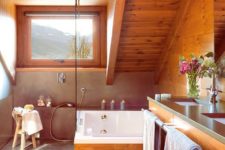 a rustic attic bathroom all clad with amber-stained wood, with a small window, a concrete shower space is very chic