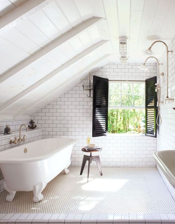 a small attic bathroom with a wooden ceiling and white subway tiles, black shutters and a vintage free-standing tub