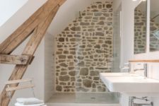 a small rustic attic bathroom with a stone wall, a wooden beam, a folding chair and a sink