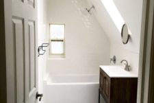 a small yet elegant white attic bathroom with various white tiles here and there, a dark vanity, a skylight for a natural feel