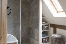 a tiny attic bathroom with a skylight, wooden beams, grey tiles and baskets for a cozy rustic feel