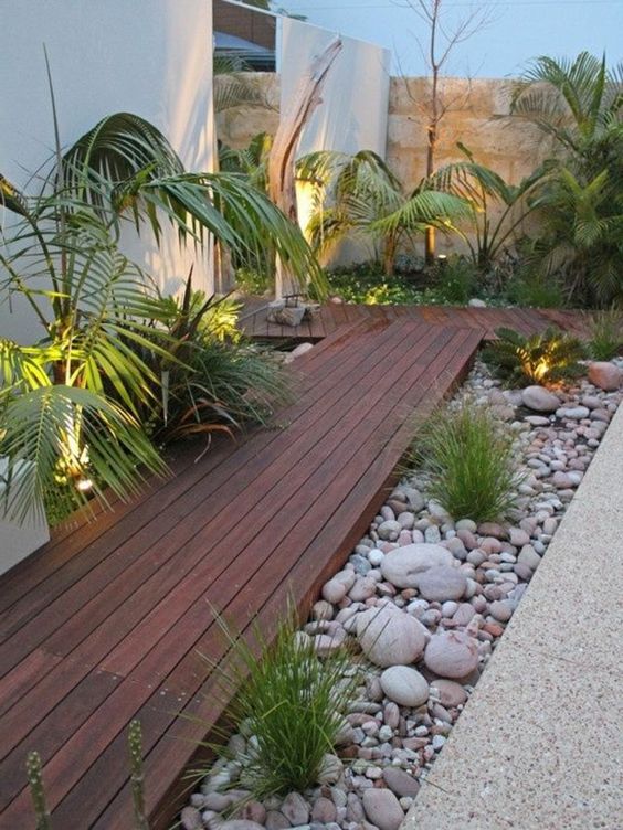 a tropical garden with pebbles covering the greenery and a rich-stained wooden pathway