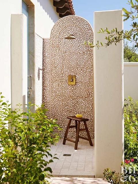 an outdoor shower with a single wall clad with pebbles and a wooden floor feels very textural and very natural