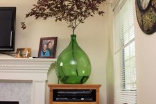 an oversized green bottle with bright leaves is a cool decoration for any space and it will bring much color