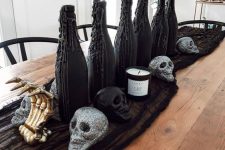 a Halloween centerpiece of black cheesecloth, glitter skulls, gilded skeleton hands, black wax bottles with greenery