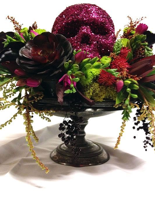 a black bowl with succulents, cascading greenery and branches, dark blooms and a sparkling red skull