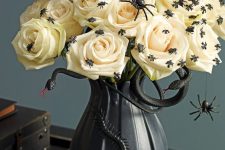a black vase with snakes and insects, white roses topped with black spiders make up a stylish centerpiece for Halloween