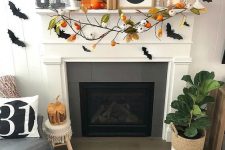 a bright Halloween mantel with a plaid sign, bats, a branch with pumpkins, mini pumpkins and candles