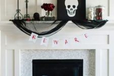 a chic Halloween mantel with bloody candles, red roses, a skull artwork, black tulle, black pillows and skeleton hands