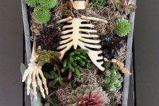 a coffin and skeleton centerpiece with succulents, moody blooms, greenery, hay and lights is a very creative idea